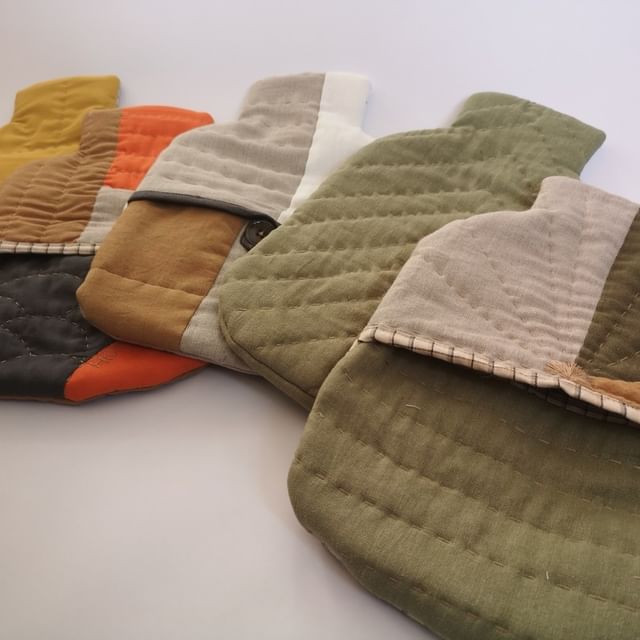 Five hot water bottles lying in a row overlapping with hand quilting details.